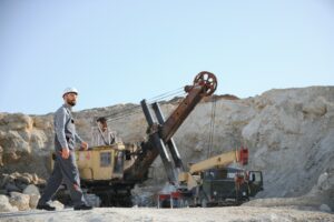 A worker in a helmet stands on the background of an excavator in a quarry