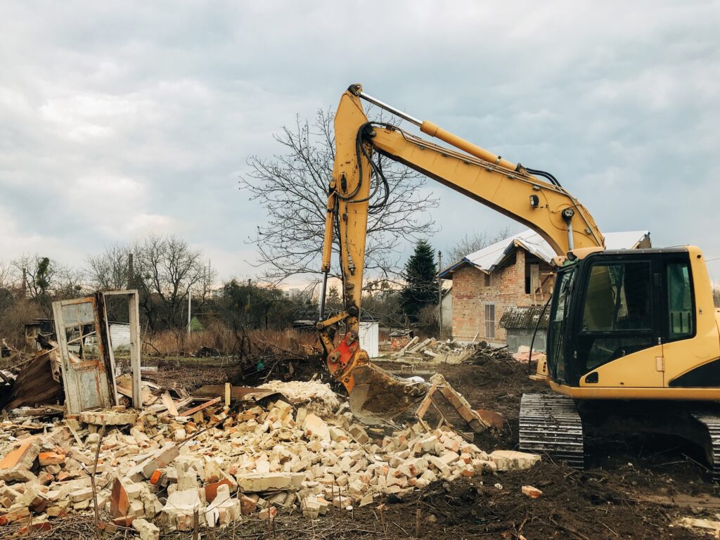 Excavator destroying brick house on land in countryside